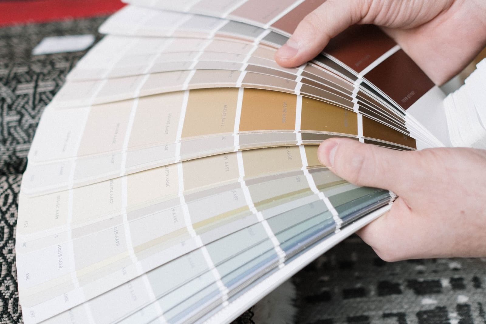 Hands fanning a deck of color swatches over upholstery fabric samples