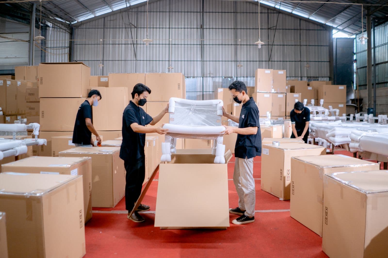 Warehouse staff packing an upholstered furniture piece into a shipping carton
