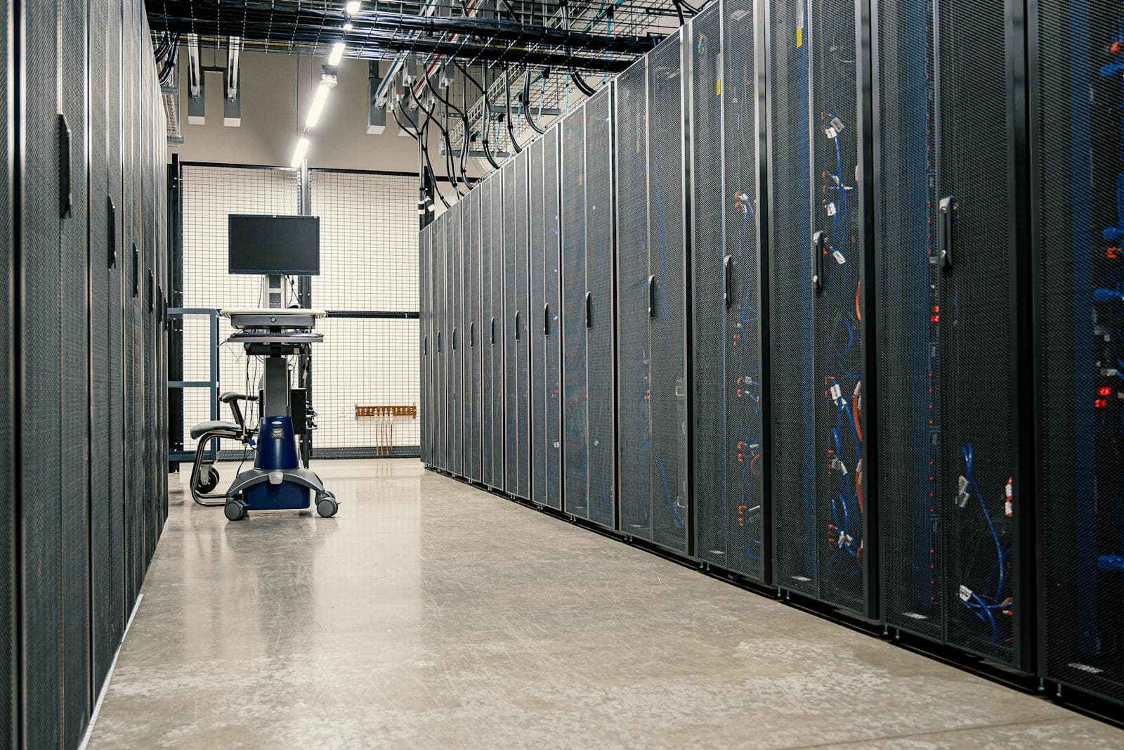 Server racks lit blue in a modern data center corridor, the physical infrastructure that absorbs traffic spikes when DDoS mitigation, autoscaling, and rate limiting are wired in correctly